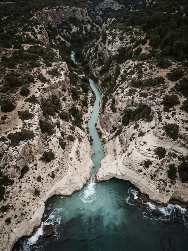 Aerial view of a white limestone gorge opening onto a turquoise Mediterranean cove